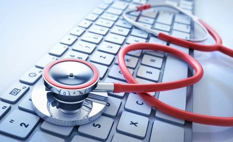 Ein Computer-Keyboard mit einem rot-silbernen Stethoskop darauf, symbolisiert Telemedizin.