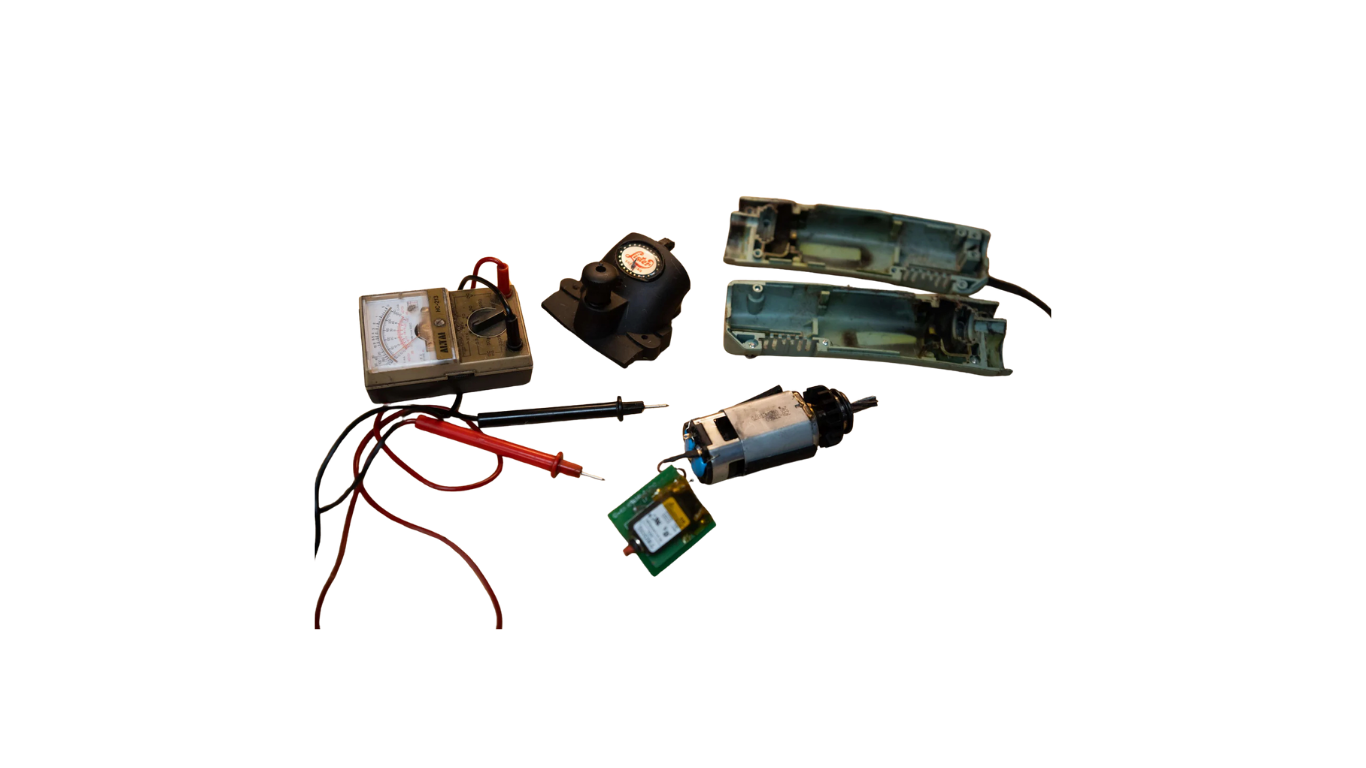 Various electronic and mechanical parts, including a gauge, wires, a small motor, and plastic components, laid out on a black background.