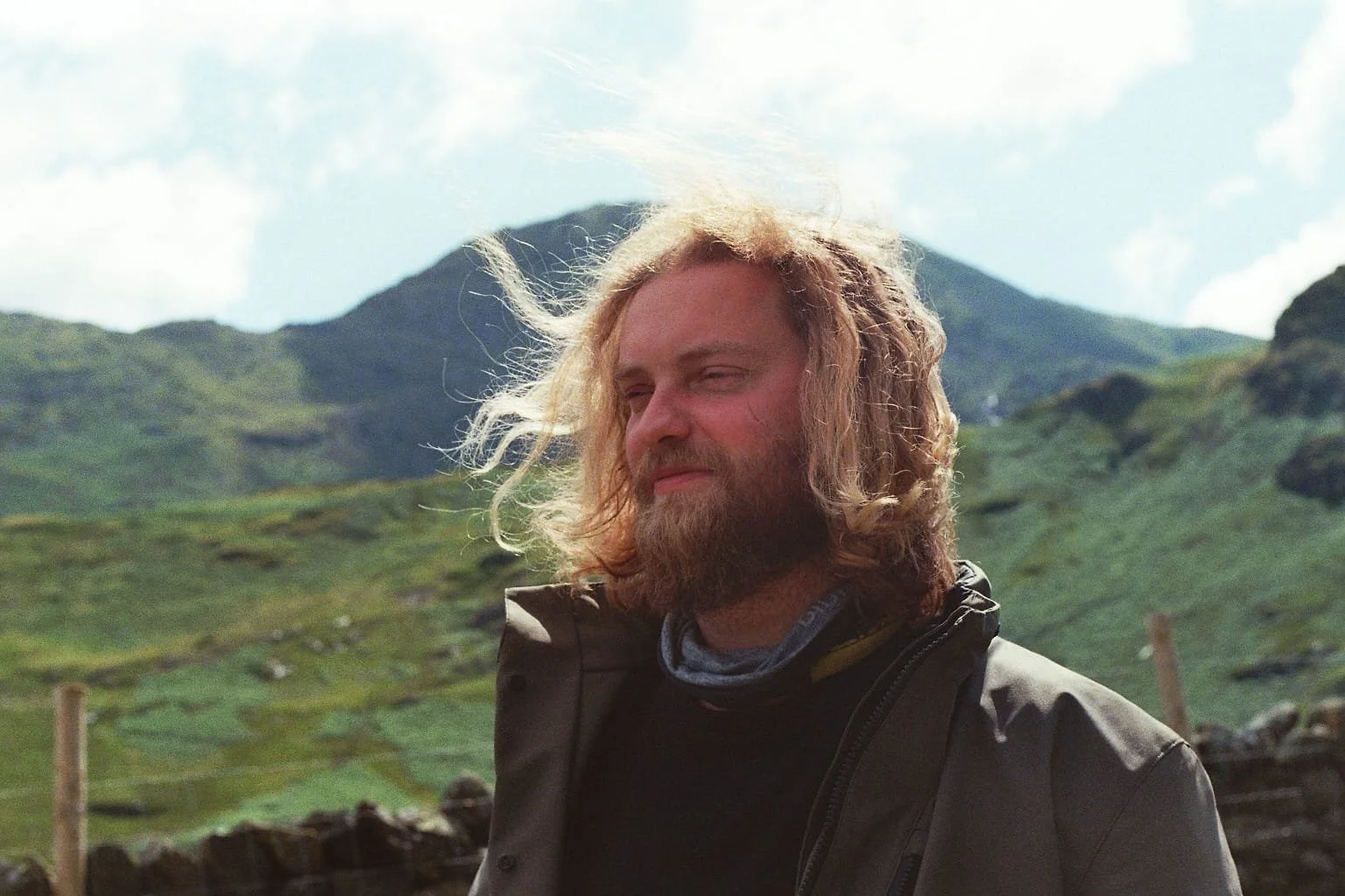 Eric de Waard met lang haar en motorjas, staat in de zon tussen de bergen in engeland