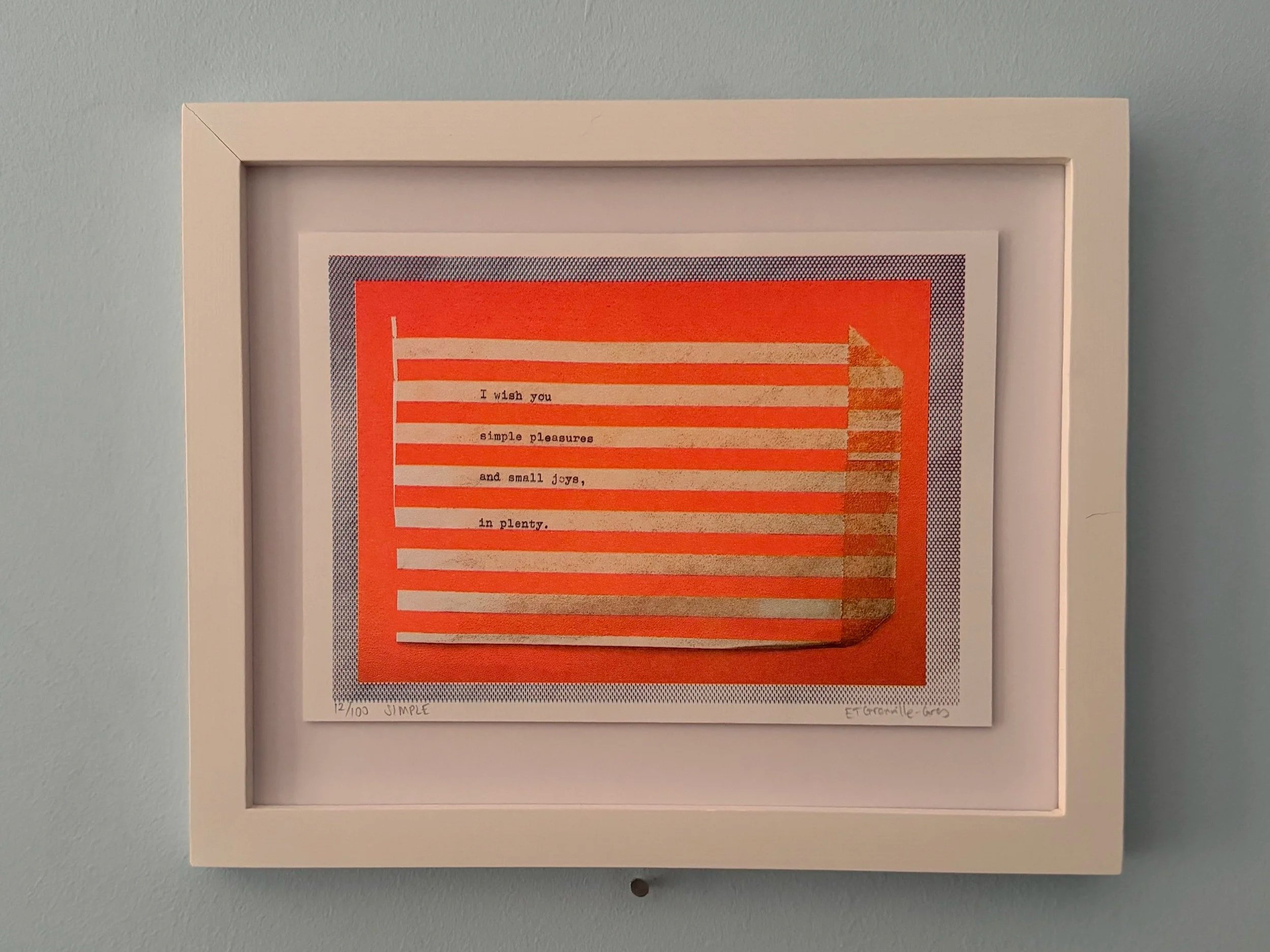 Framed artwork featuring an orange background with lines and text, displayed on a light blue wall.
