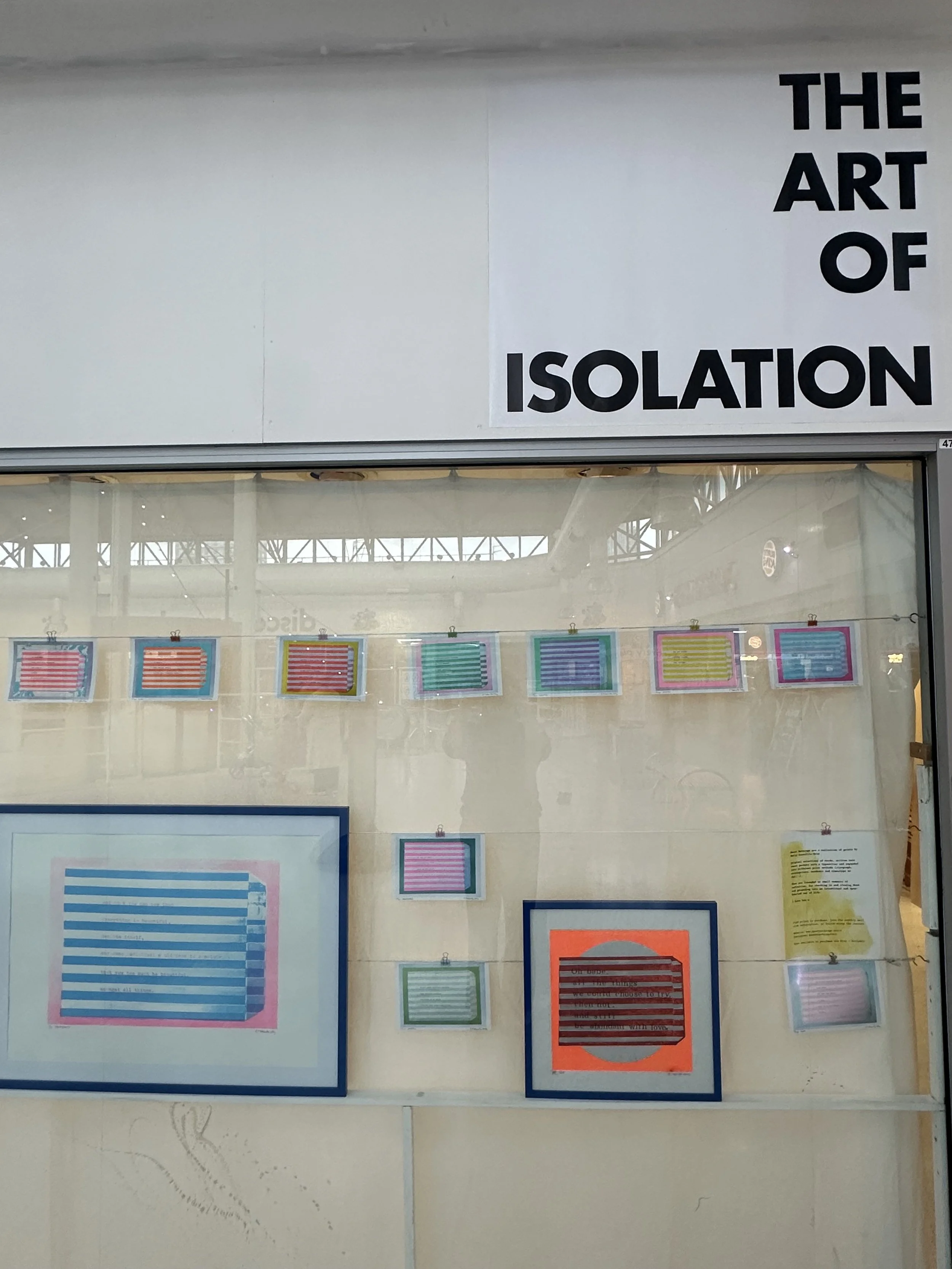 Display window with various colorful striped artworks and a sign that reads "The Art of Isolation".