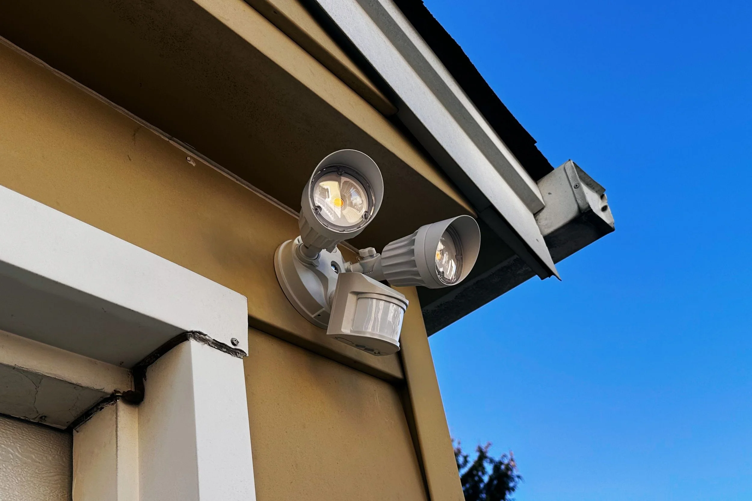 A security camera with two LED lights mounted on the corner of a building under a blue sky.