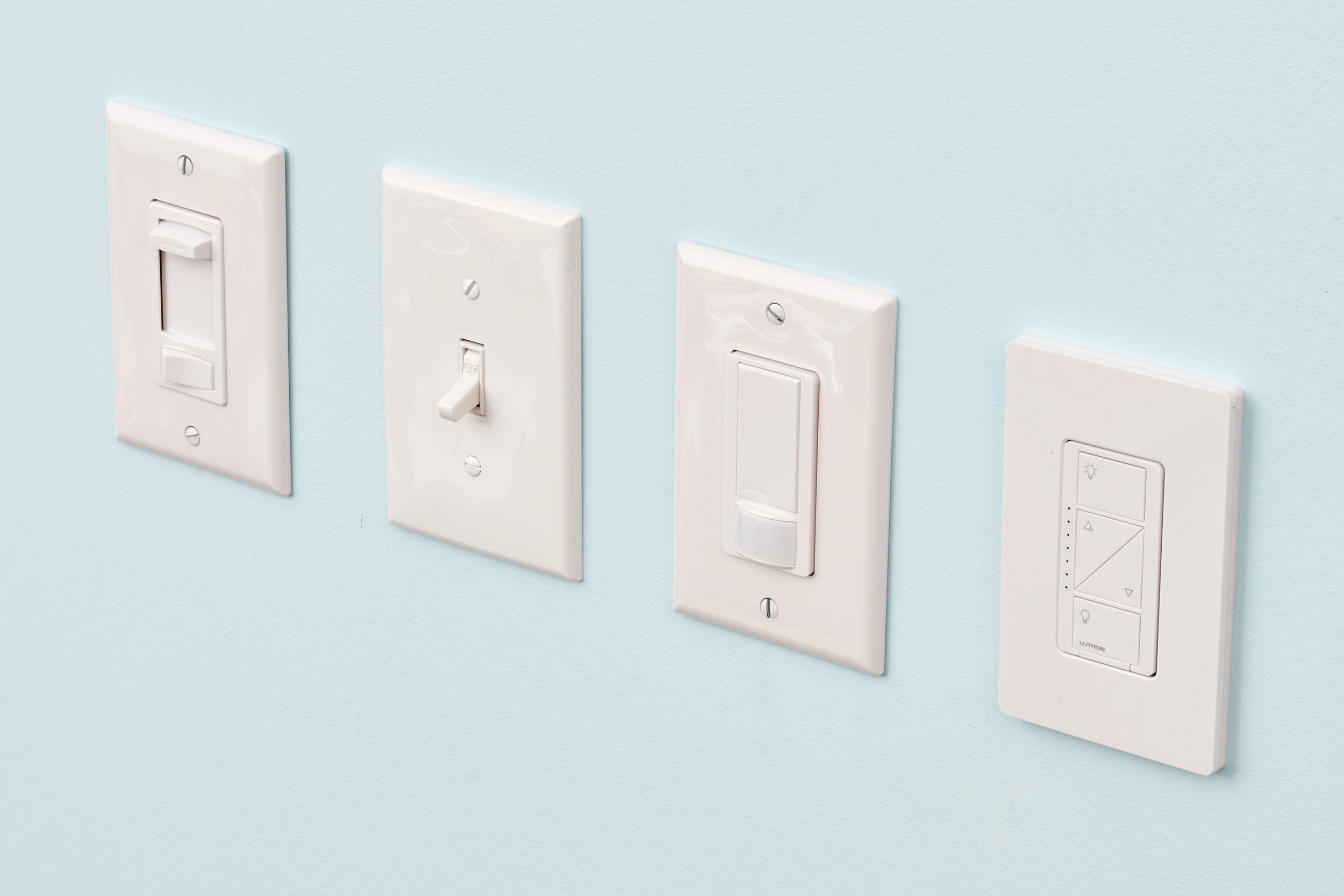 Four white light switches on a light blue wall, each with different designs and functions.