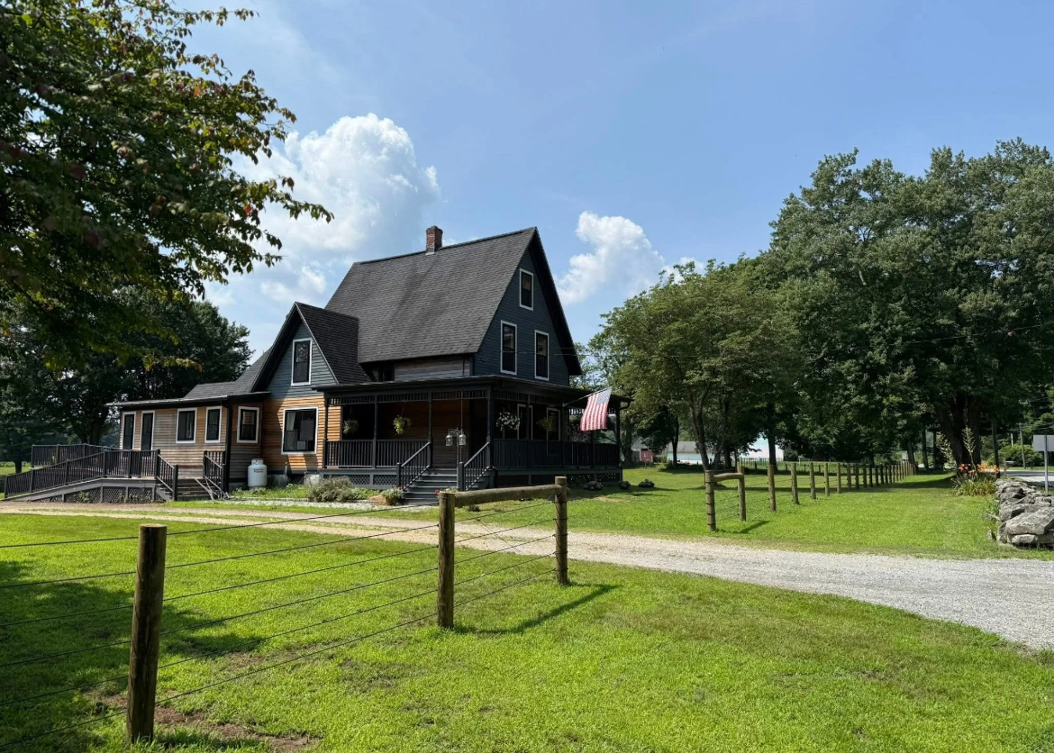 A large two-story house painted in black with a covered front porch surrounded by greenery and trees, under a partly cloudy sky. farmhouse connecticut family owned farm and dog breeder near me cavapoos