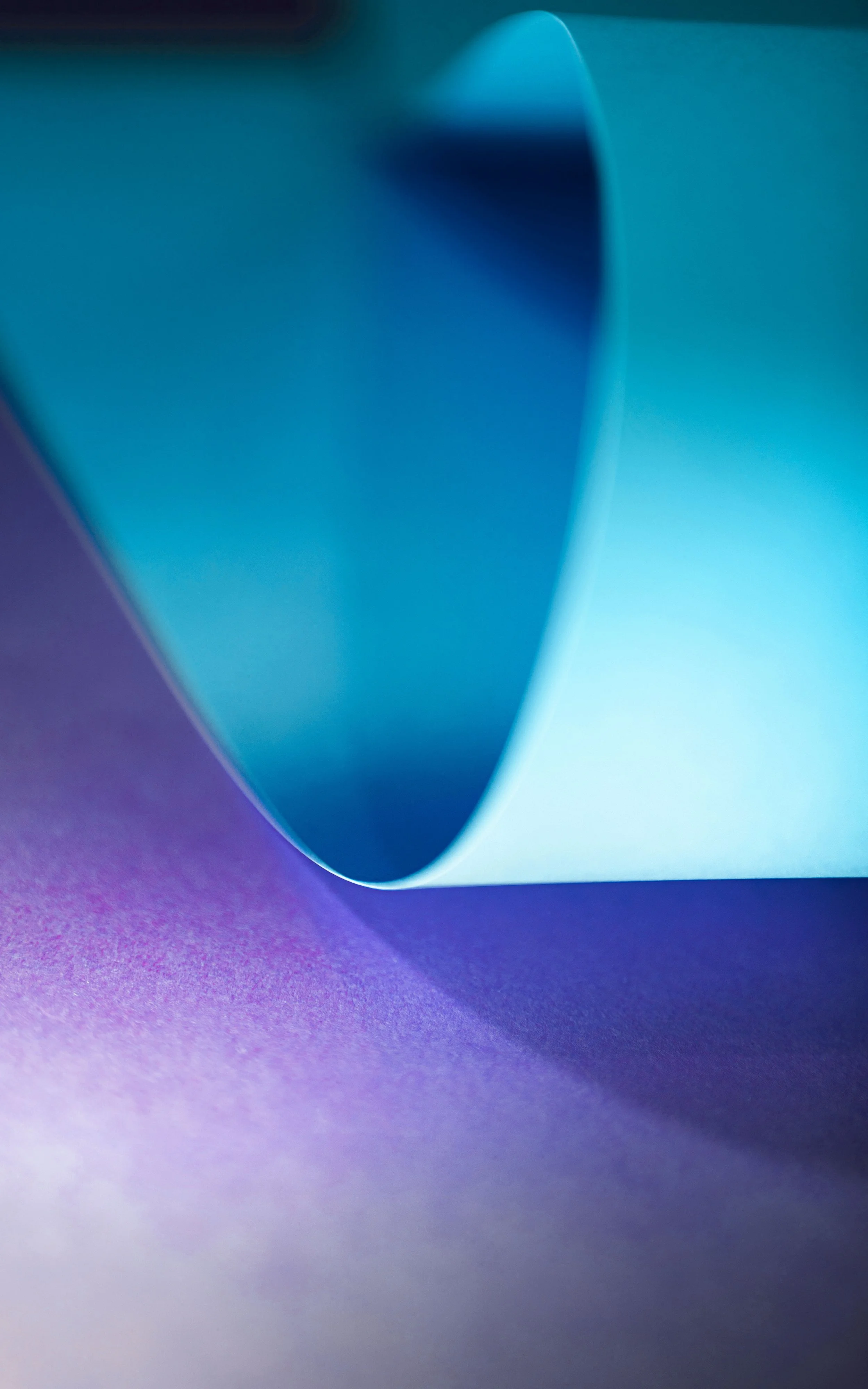 Close-up of a blue paper sheet curling over a purple textured surface.