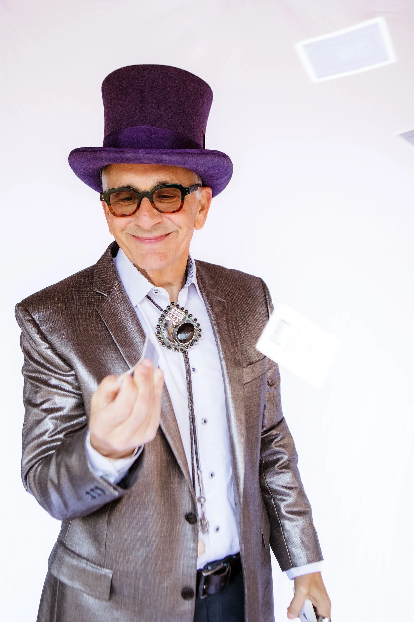 Peter Zandan a.k.a. The Great Zandini in purple top hat, bolo tie and shimmery champagne jacket shuffling cards