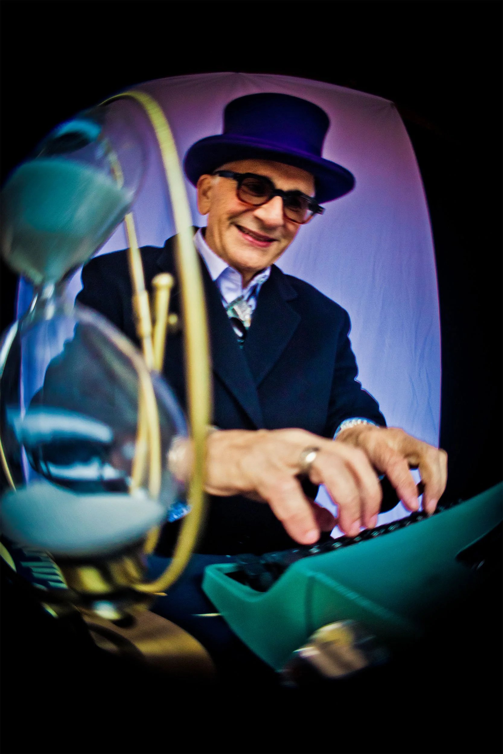 A man wearing a top hat, glasses, and a suit, smiling and typing on a typwriter, with an hourglass in the foreground.