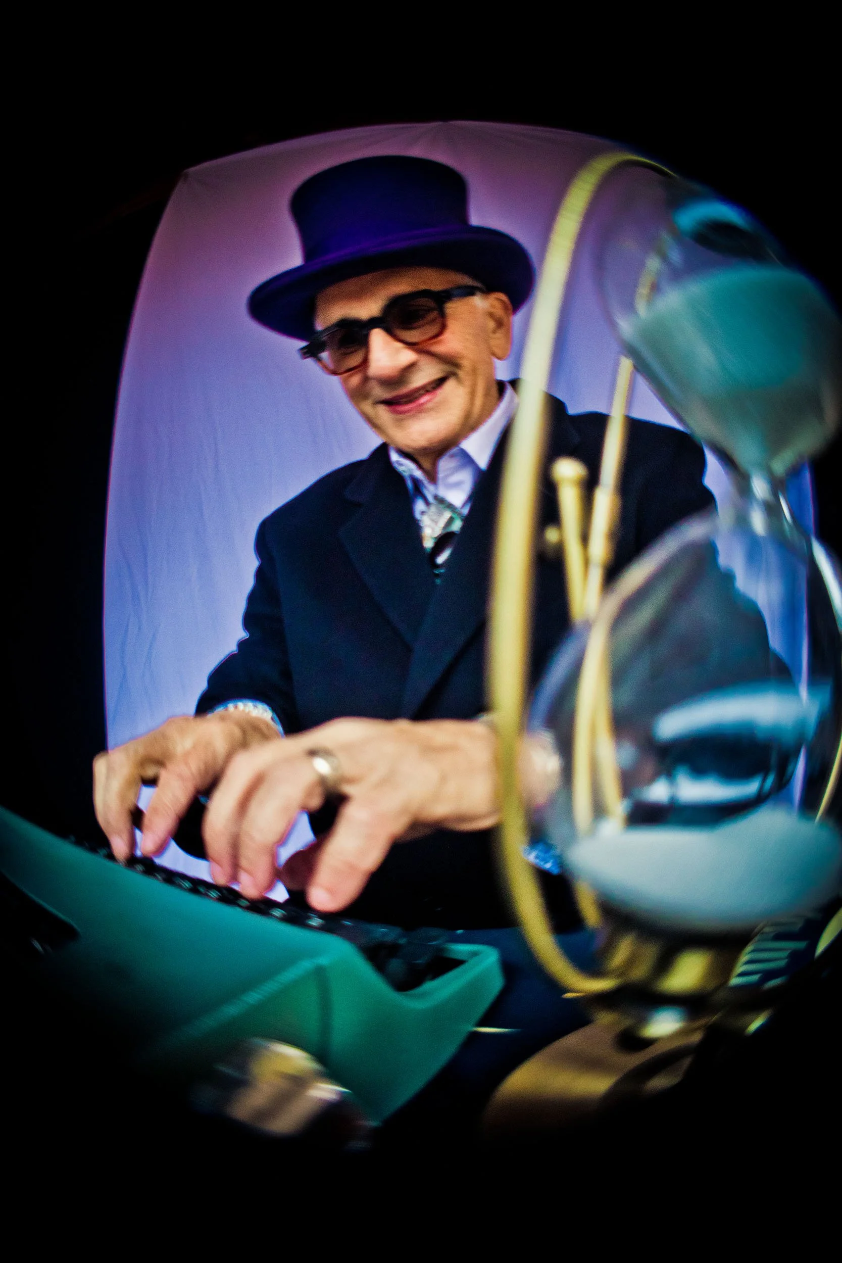 Peter Zandan a.k.a. The Great Zandini in purple top hat and coat typing on green typewriter  with green hourglass in foreground