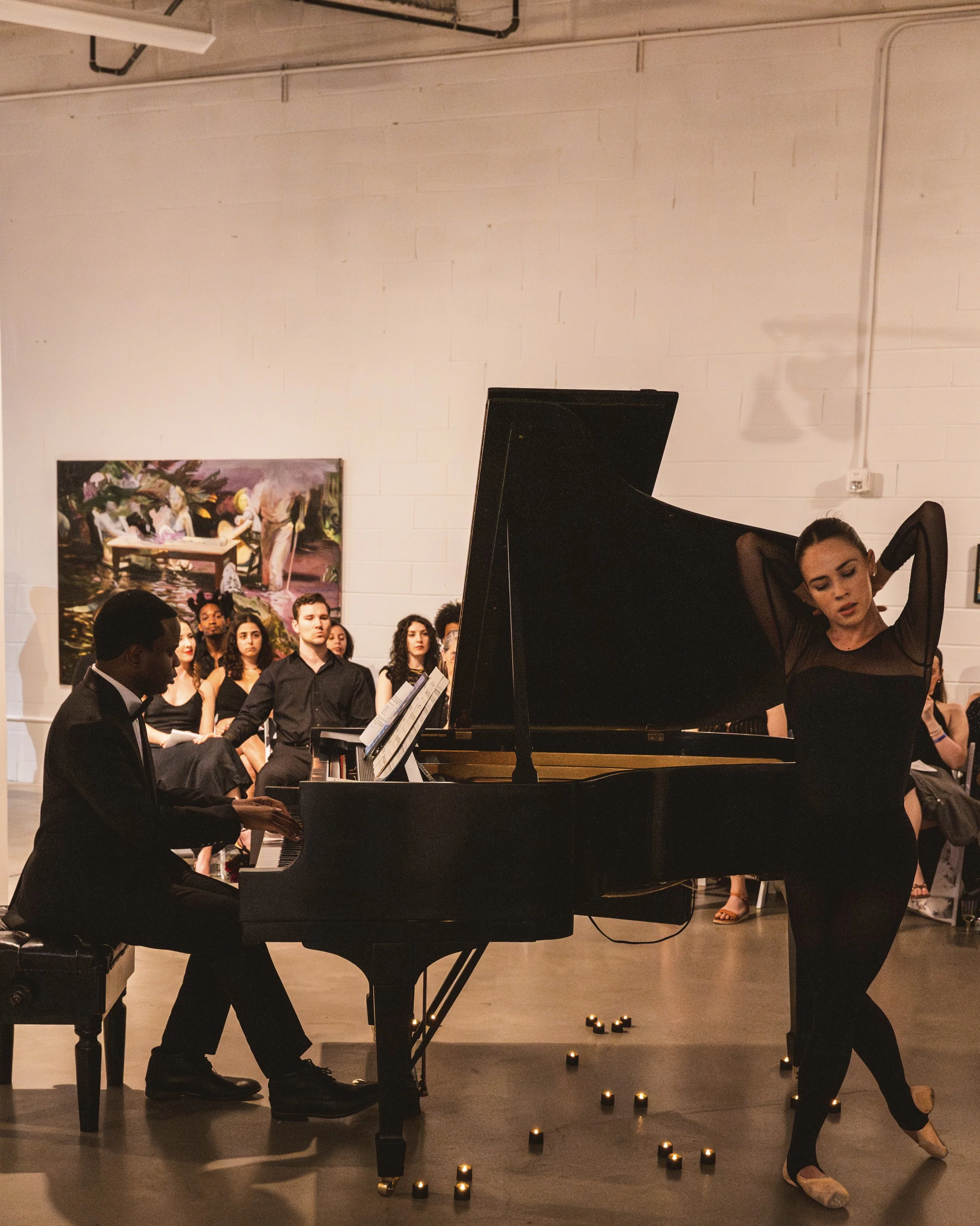 A pianist playing a grand piano and a ballet dancer performing in front of an audience during a dance event.