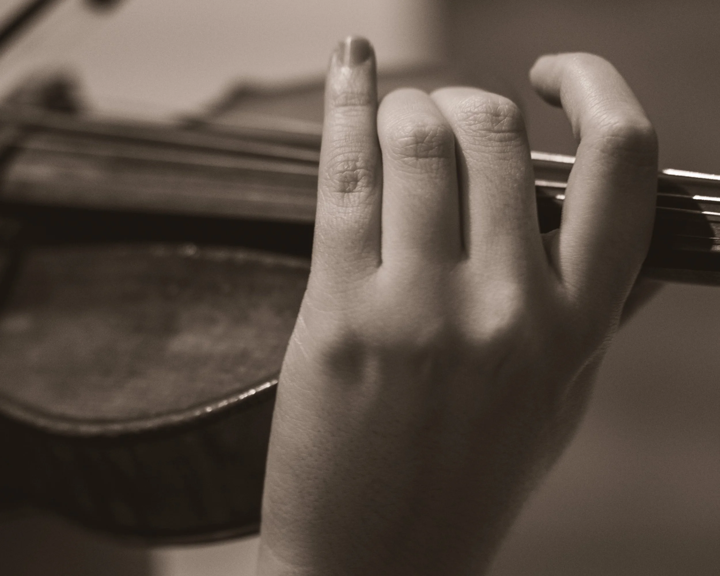 A hand holding a violin bow with a book in the background