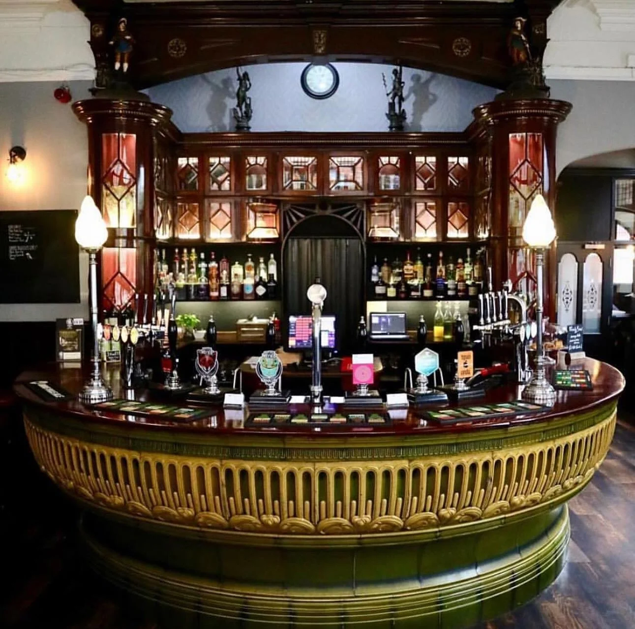 Elegant wooden bar with illuminated taps, bottles on shelves, and decorative wooden accents in a cozy pub setting.
