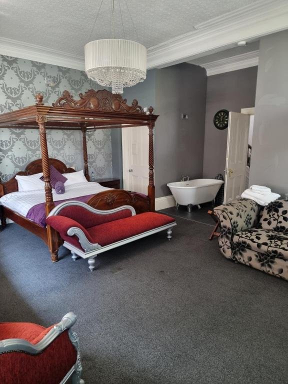 Hotel room with a four-poster bed, velvet bench, patterned sofa, and a bathtub next to the wall.