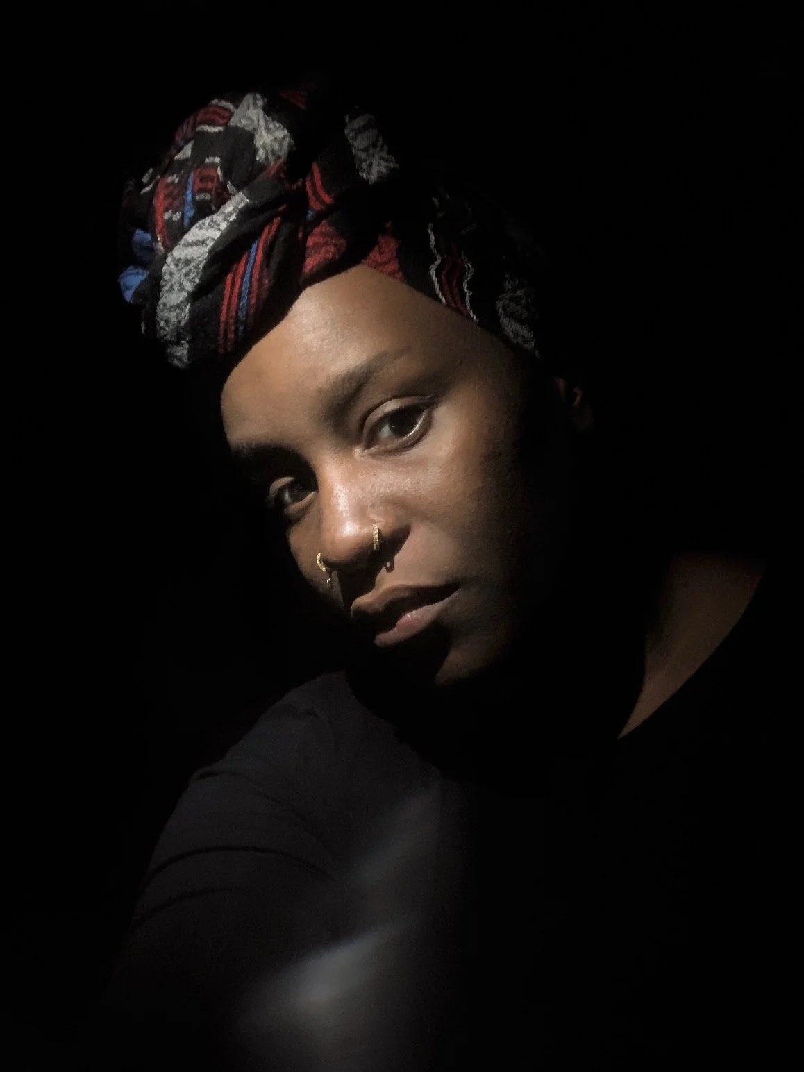 Portrait of a woman wearing a colorful headwrap with dark background