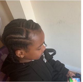 A young girl with braided hair sitting in a chair, looking at a mobile device in her hands.