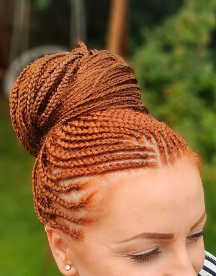 Woman with intricately styled ginger braids in a high bun outdoors.