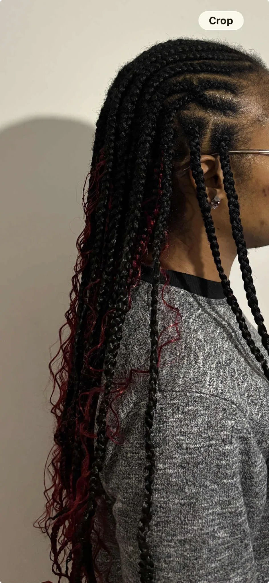 Side view of a person with long braided hair, some braids have red curls, wearing glasses and a gray sweater.