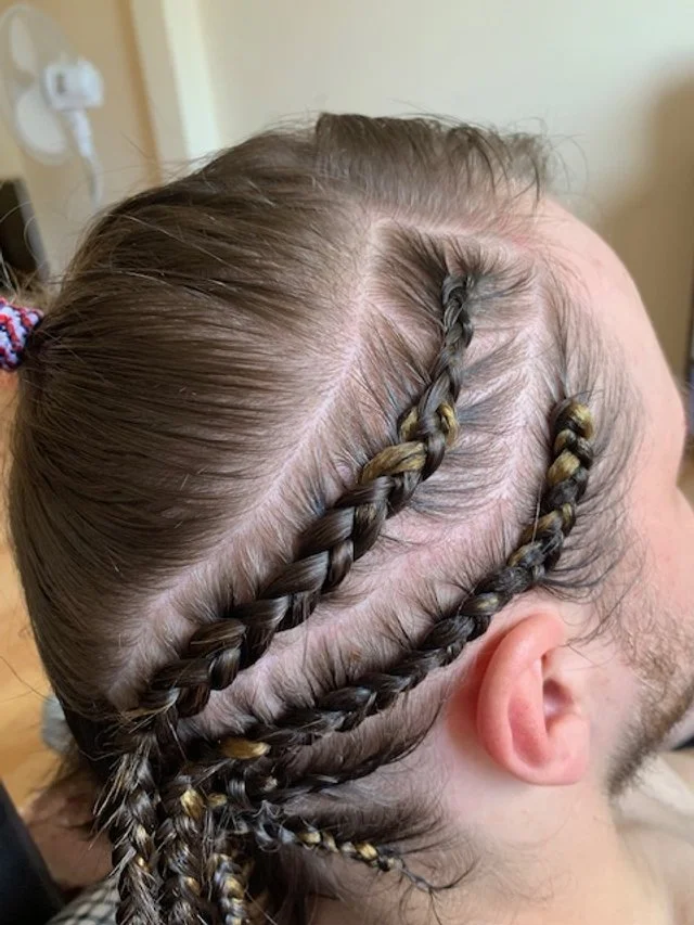 Close-up of a person's head showing braided hairstyle on the scalp with multiple tight braids and hair extensions.