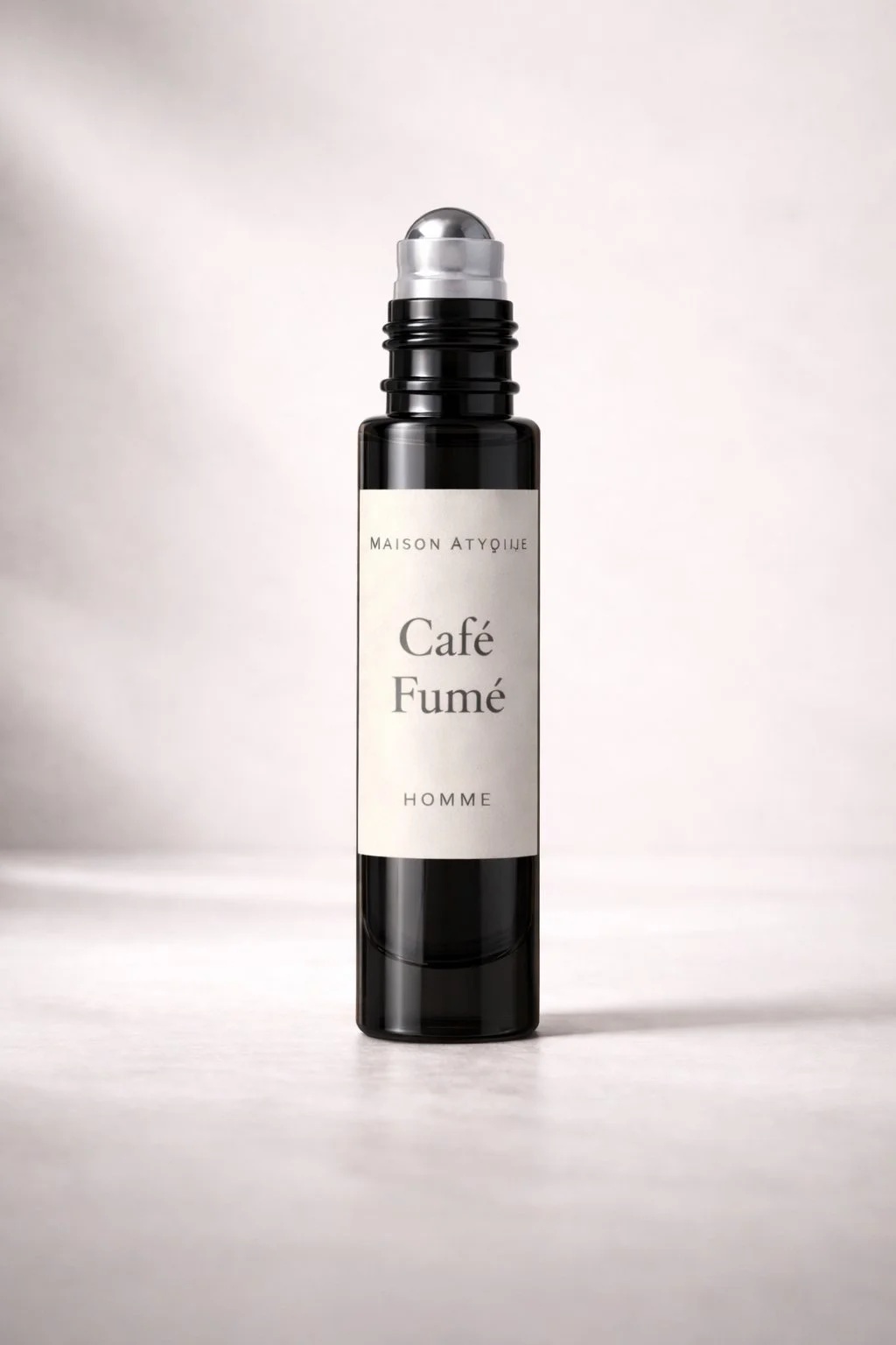 A black cylindrical bottle with a silver rollerball top, labeled 'Maison Atqije Café Fumé Homme,' against a neutral background.