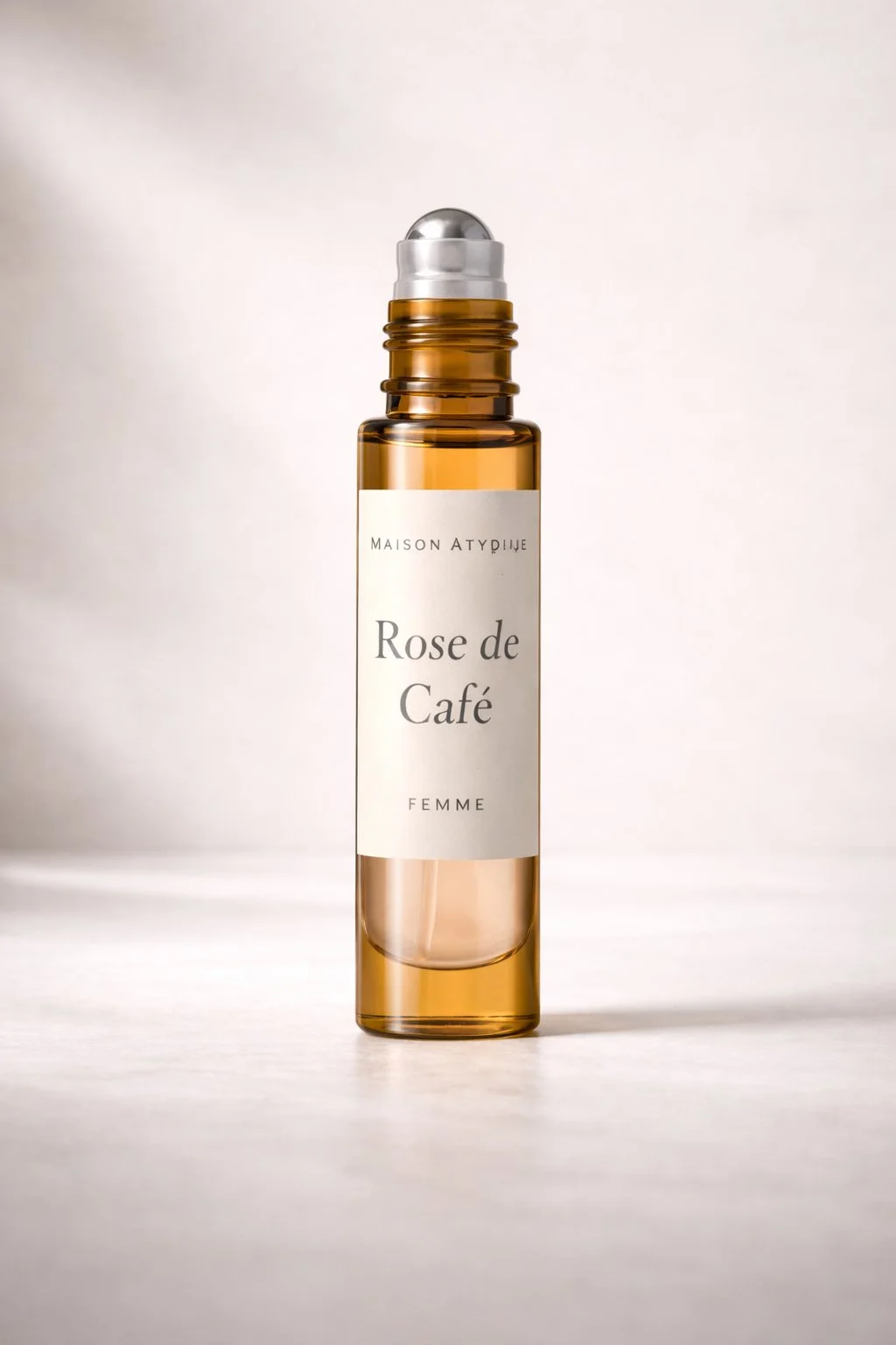 A perfume bottle labeled 'Maison Atipique Rose de Café Femme' with a rollerball applicator, set against a neutral background.