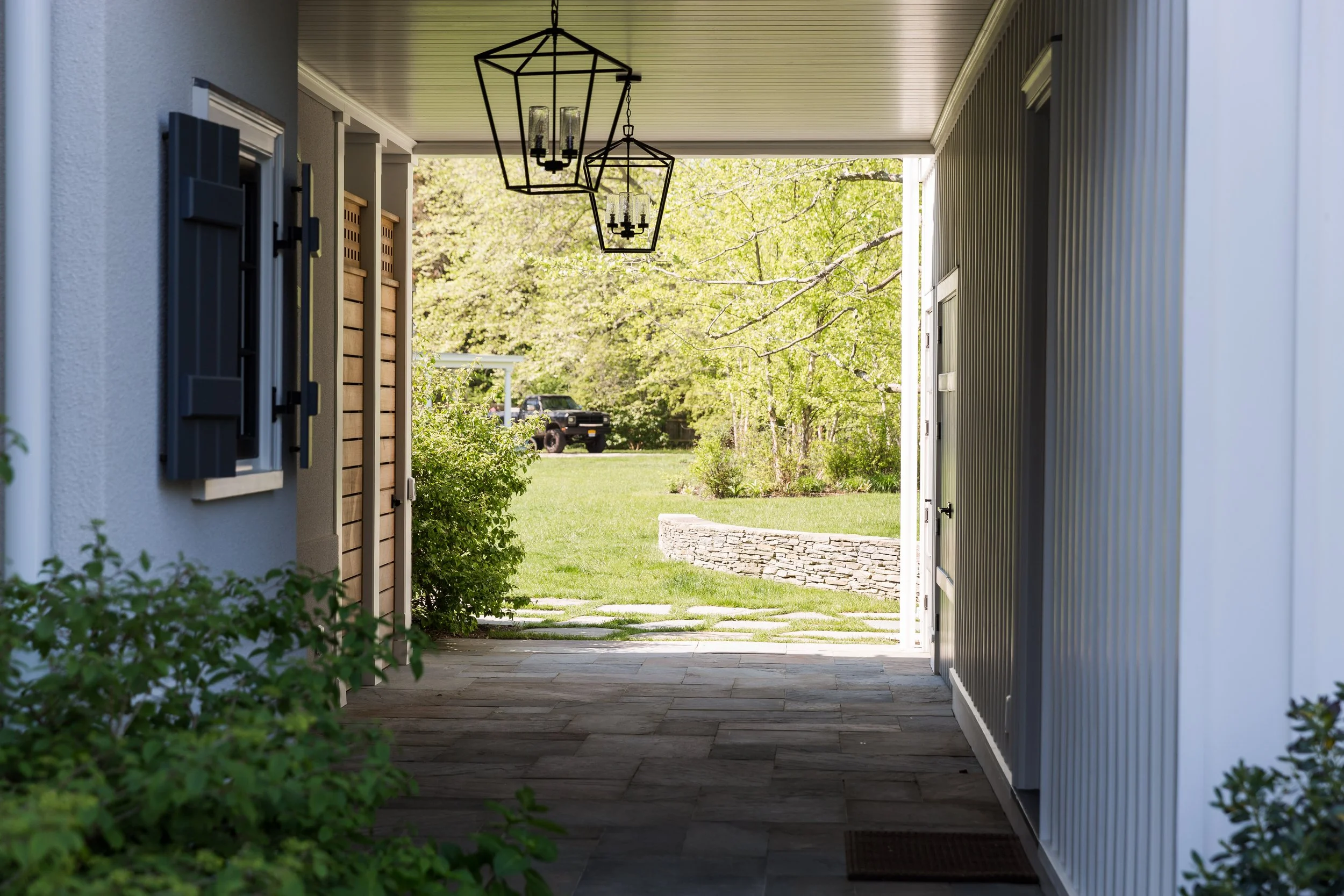 View from inside a covered porch looking out to a grassy yard with trees and a stone-bordered garden bed, with a vintage black truck in the distance.