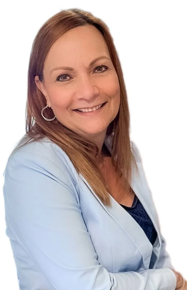 A woman with long reddish-brown hair smiling, wearing a light blue blazer and hoop earrings, against a white background.