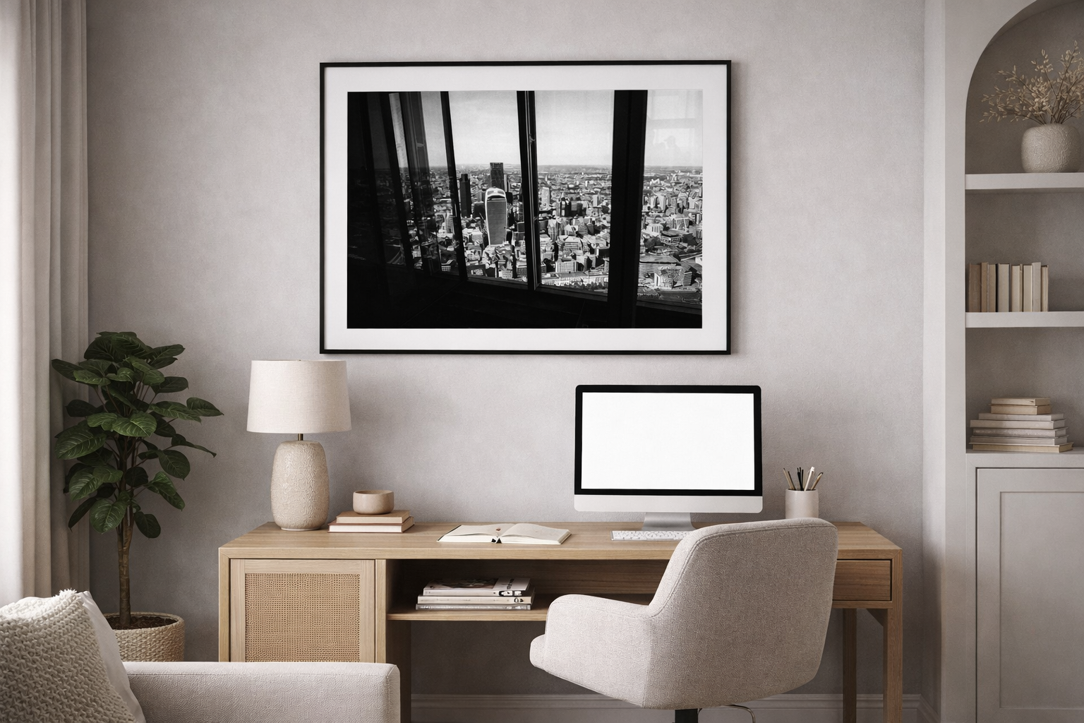A modern home office with a wooden desk, beige chair, computer monitor, houseplant, lamp, and framed cityscape photograph on the wall.
