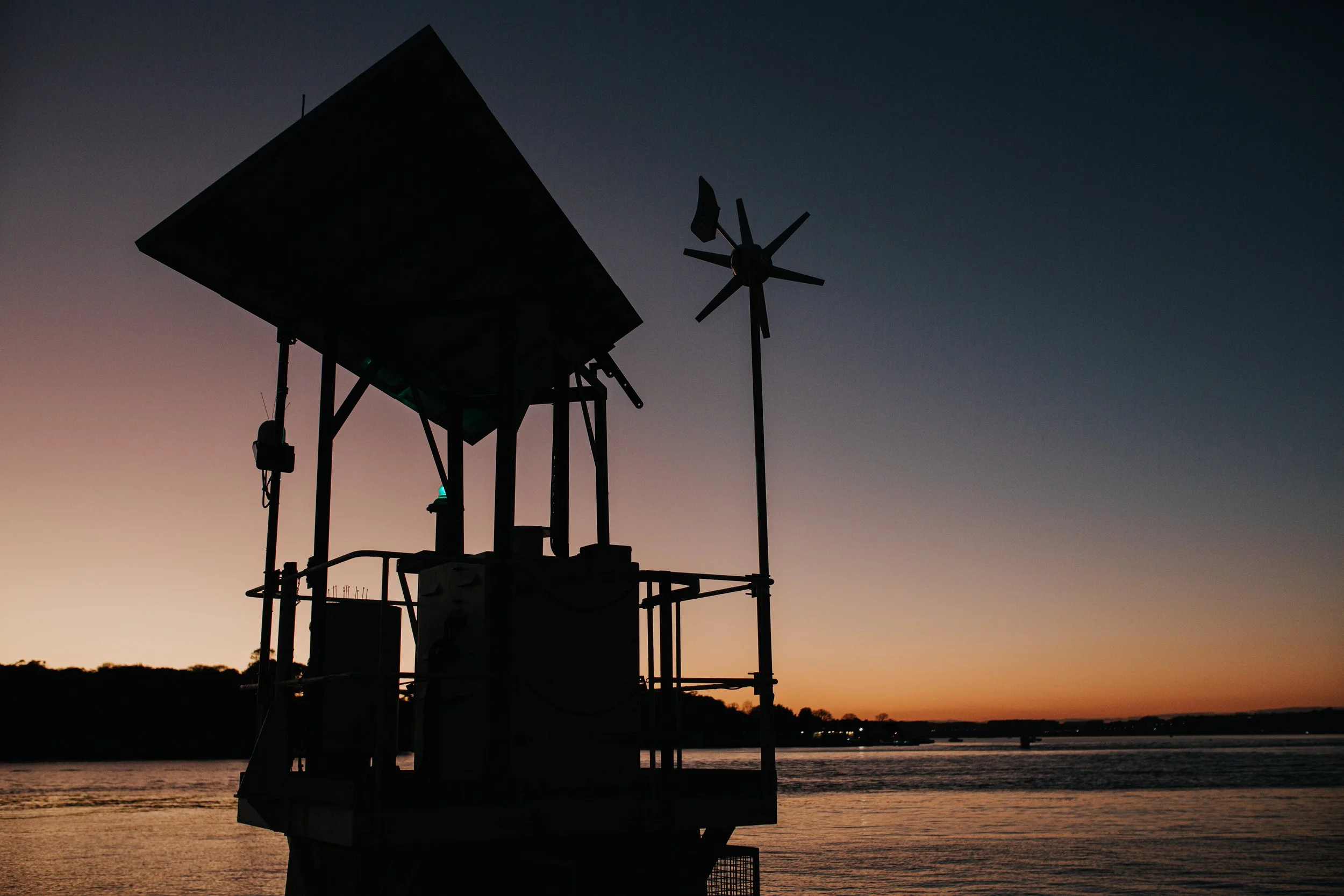 Silhouette of a water tower and a weather vane at sunset over a body of water.