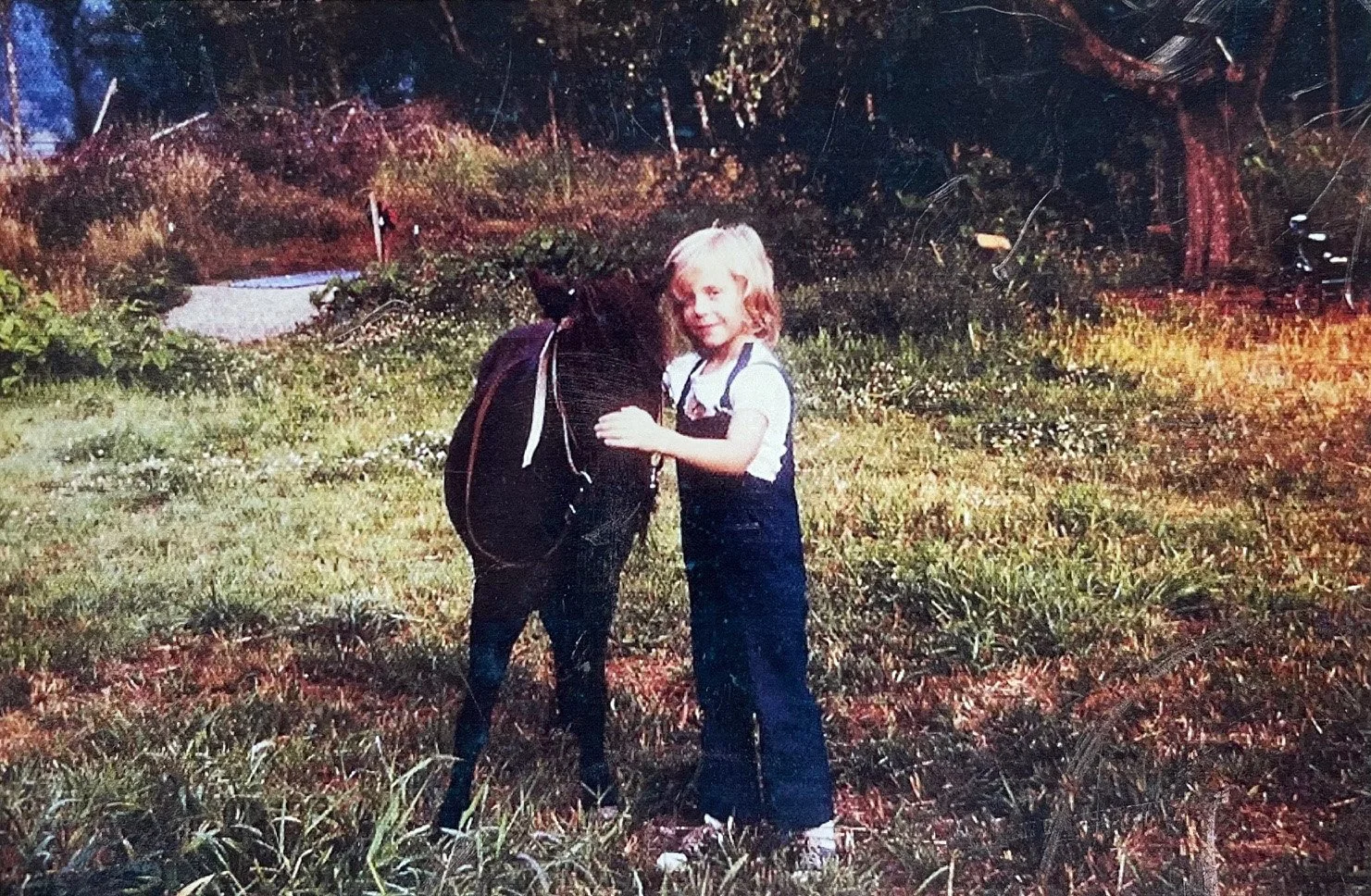 Young Gabrielle and her pony Skipper standing in a field together.