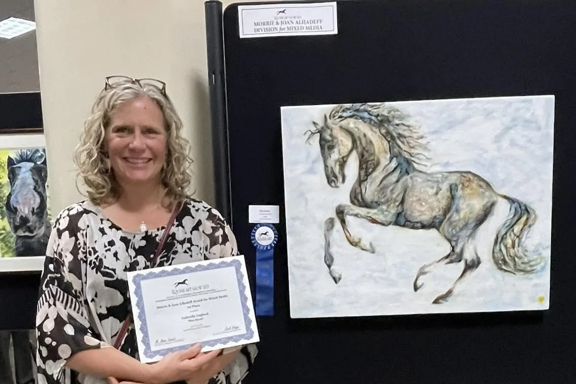 Gabrielle England holding an award ribbon besides her horse painting at an art exhibition.