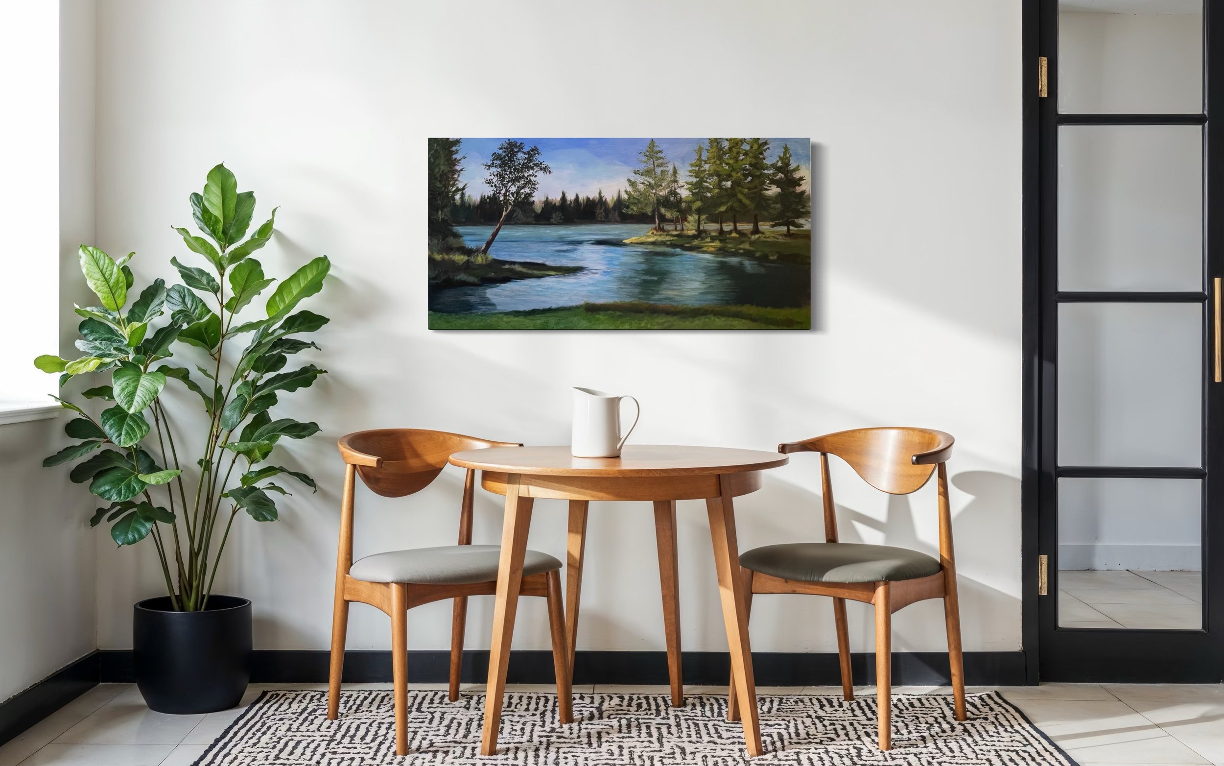 Interior dining area with a round wooden table, two matching wooden chairs with upholstery, a large potted plant on the left, a landscape painting of a river and trees on the white wall, a black door with glass panel on the right, and a patterned rug on the floor