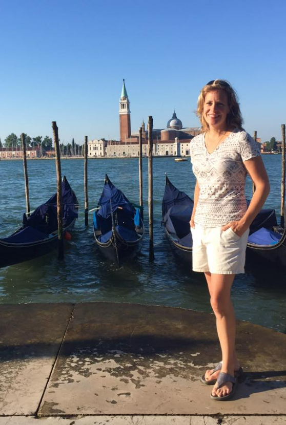 Gabrielle England standing by gondolas on the waterfront in Venice, Italy.