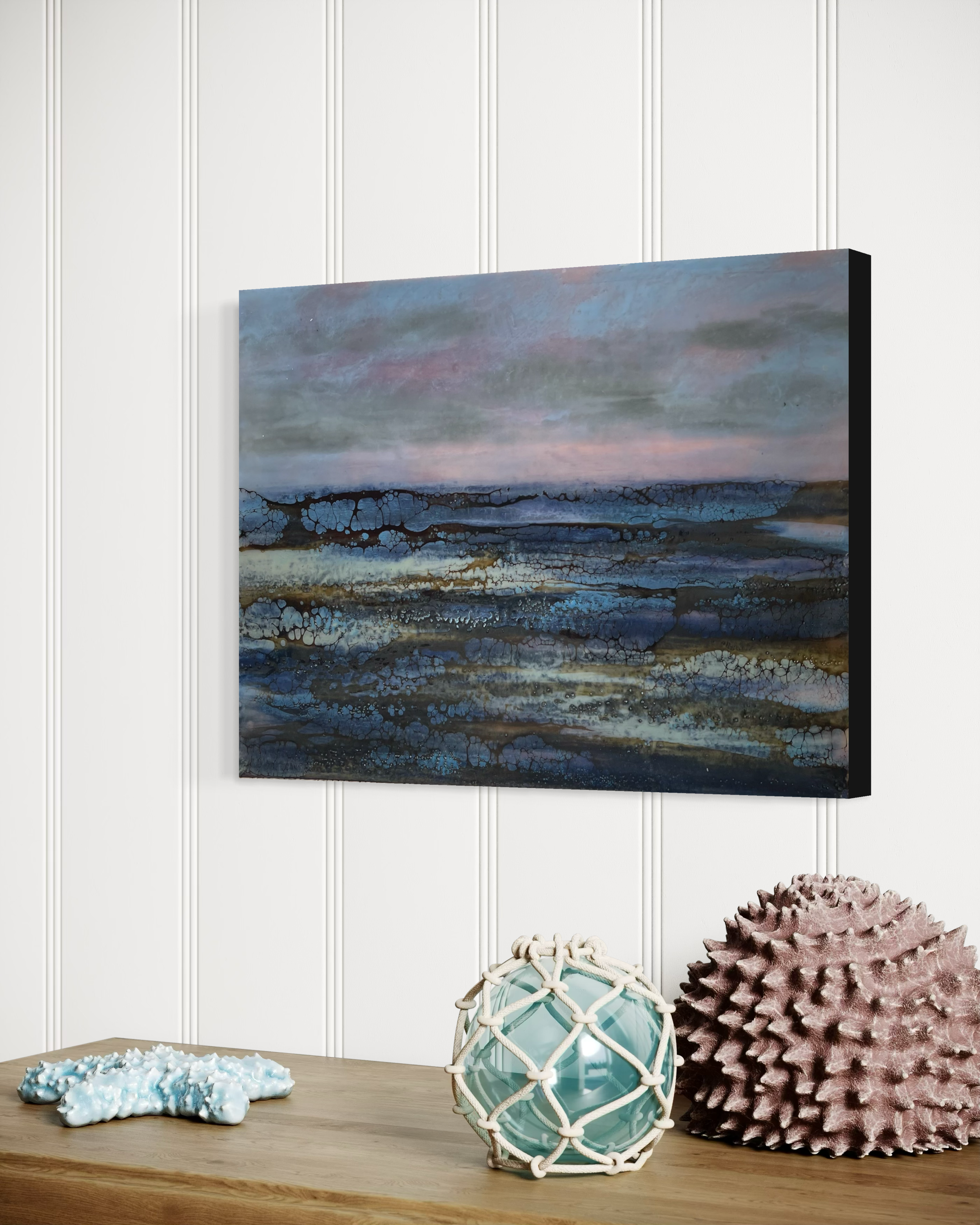 Quiet Seas encaustic painting displayed above a shelf with coastal decor in a minimalist interior.