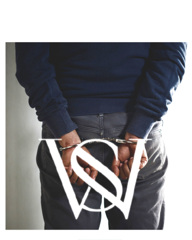 Person in a navy blue hoodie and gray pants handcuffed behind their back, with a white stylized 'V' and 'S' logo overlayed at the bottom.