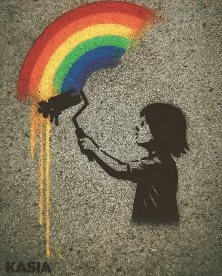 Street art of a young girl spray painting a rainbow, with her silhouette in black spray paint on a rough wall.