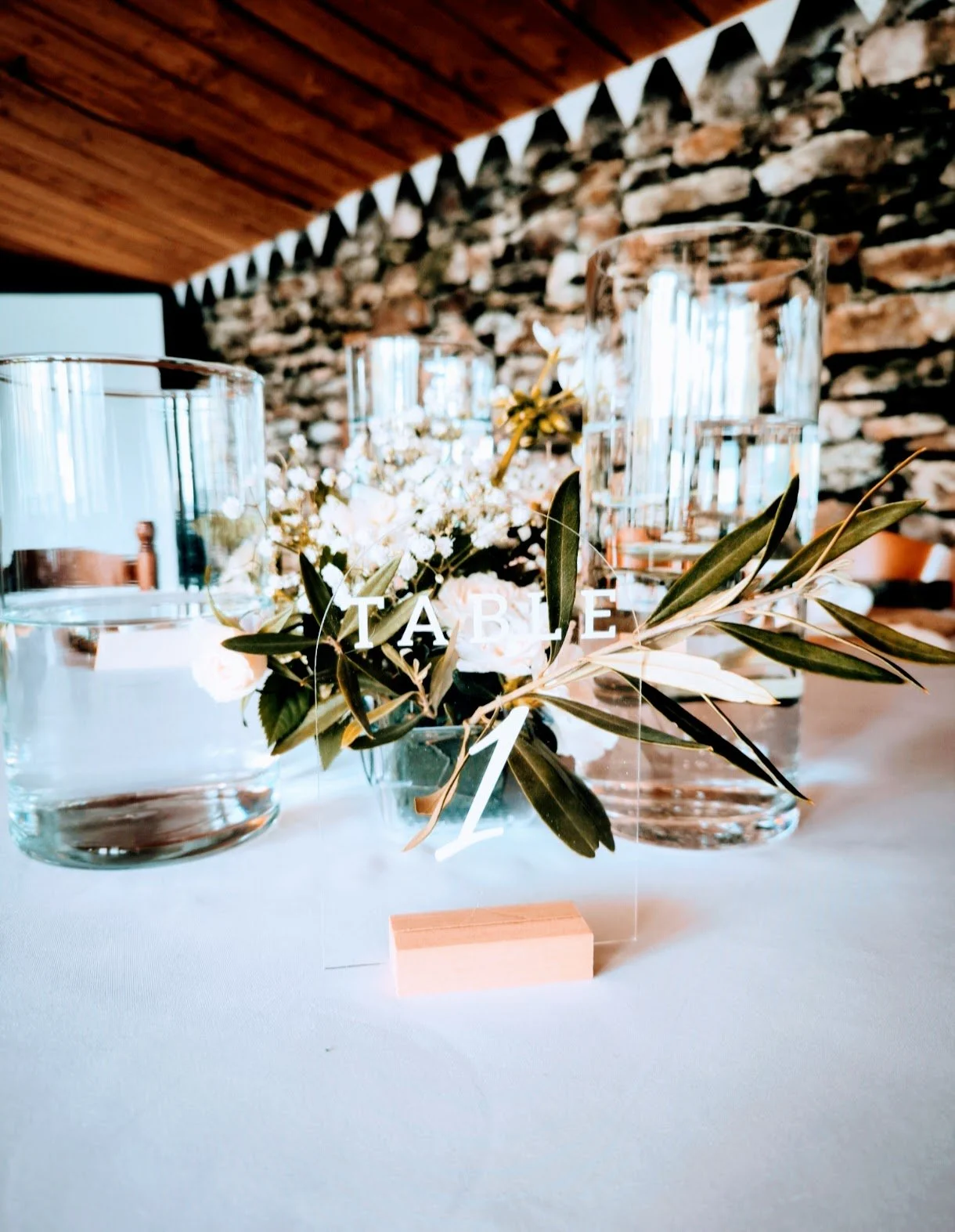 Centre de table avec fleurs blanches et feuillage vert, flacons d'eau en verre, décorations pour un mariage ou un événement.