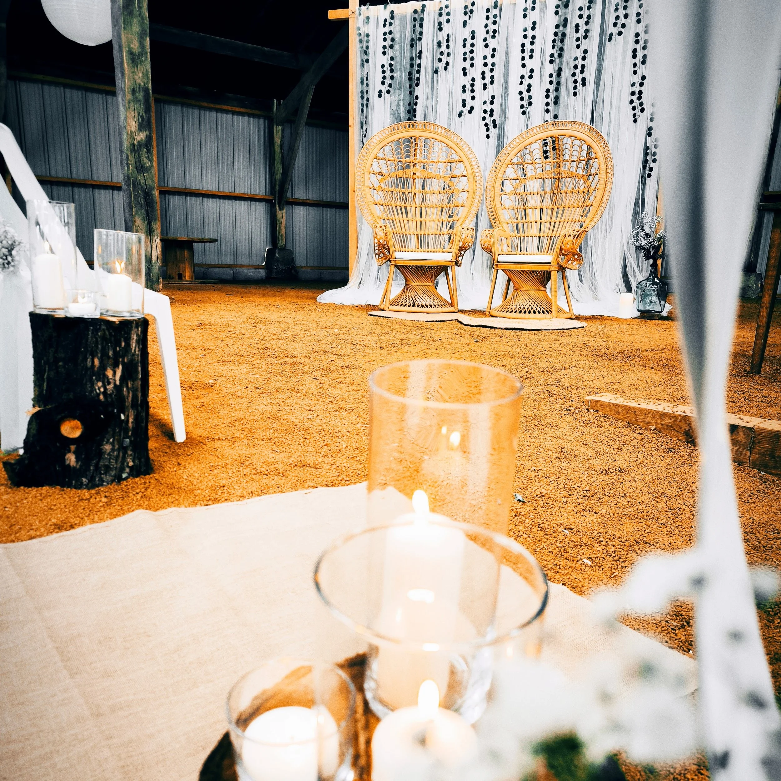 Deux fauteuils en rotin style papasan à l'arrière-plan devant une toile blanche avec des motifs noirs, décorés de bougies et de fleurs en vases, dans un cadre intérieur à l'ambiance chaleureuse.