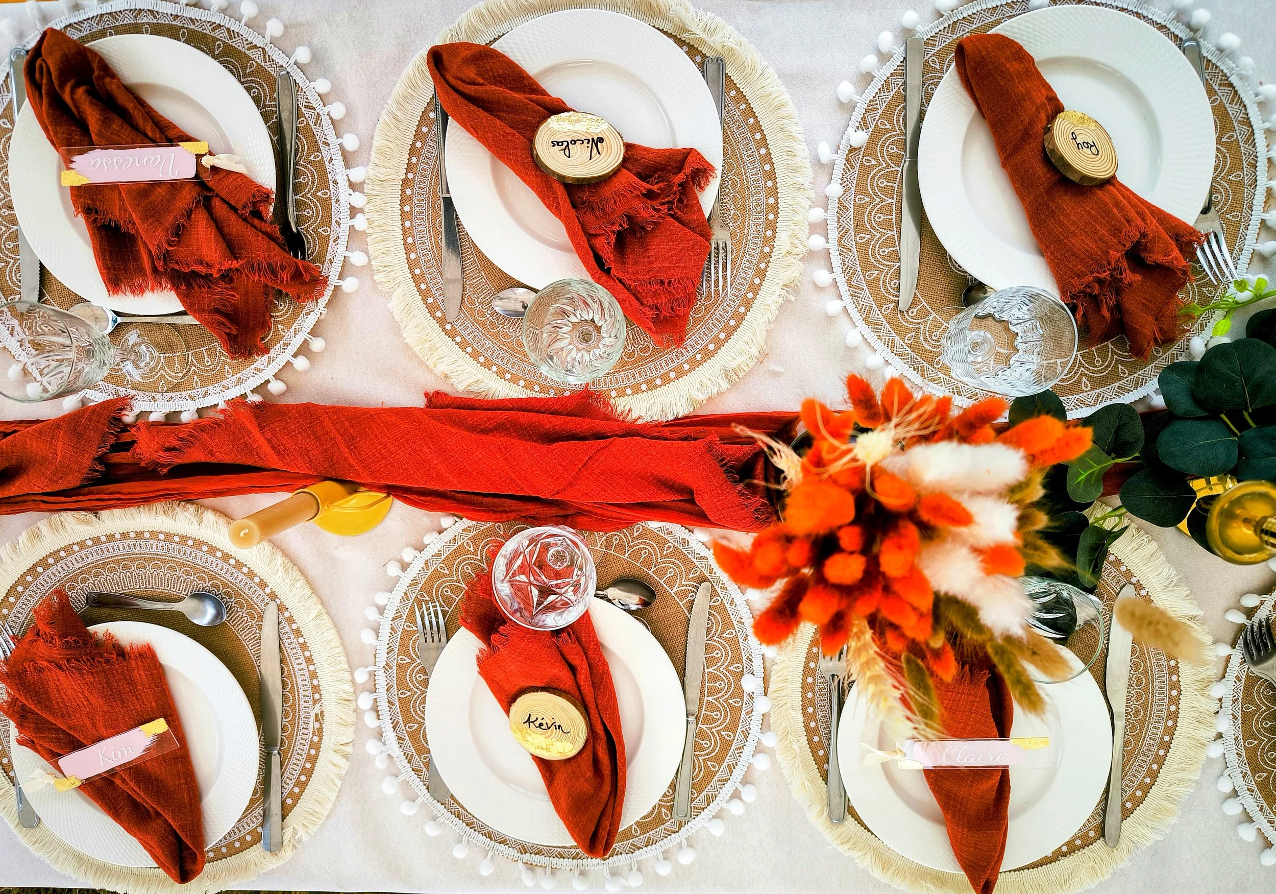 Table de fête style terra cotta avec des assiettes, des verres, des couverts et des serviettes rouges, ornée de centres de table avec des fleurs rouges, oranges et blanches.