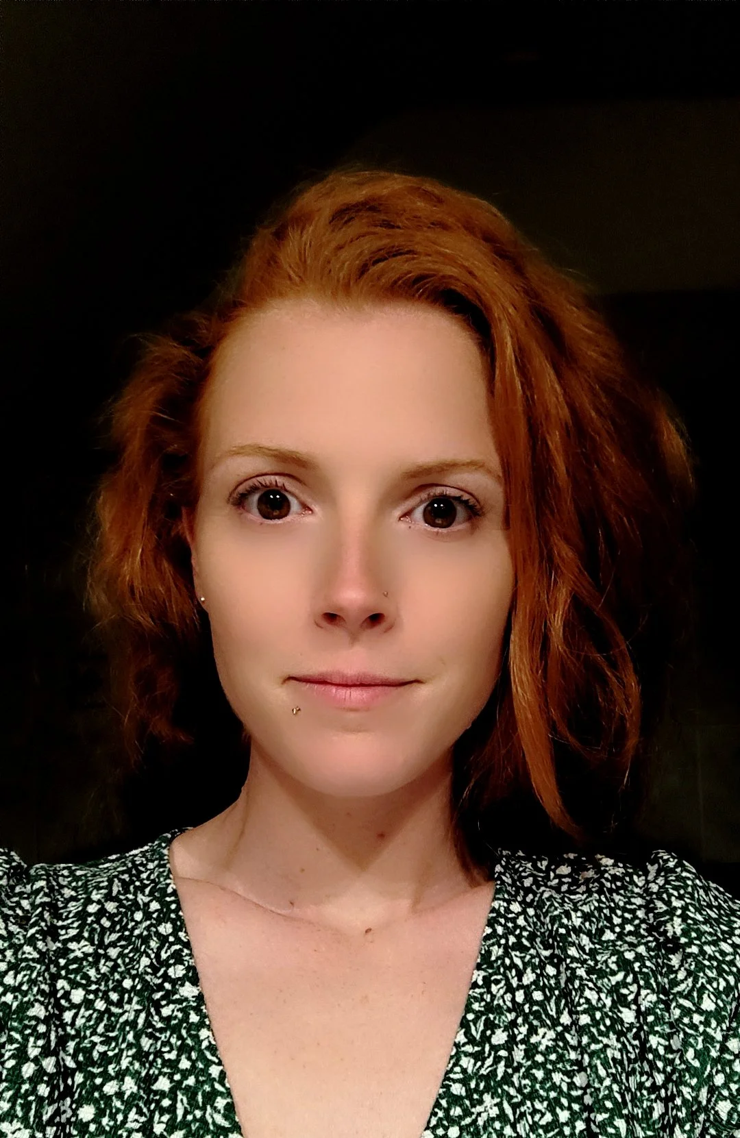 Portrait d'une femme avec des cheveux roux, portant un haut à motifs verts et blancs, face à la caméra.