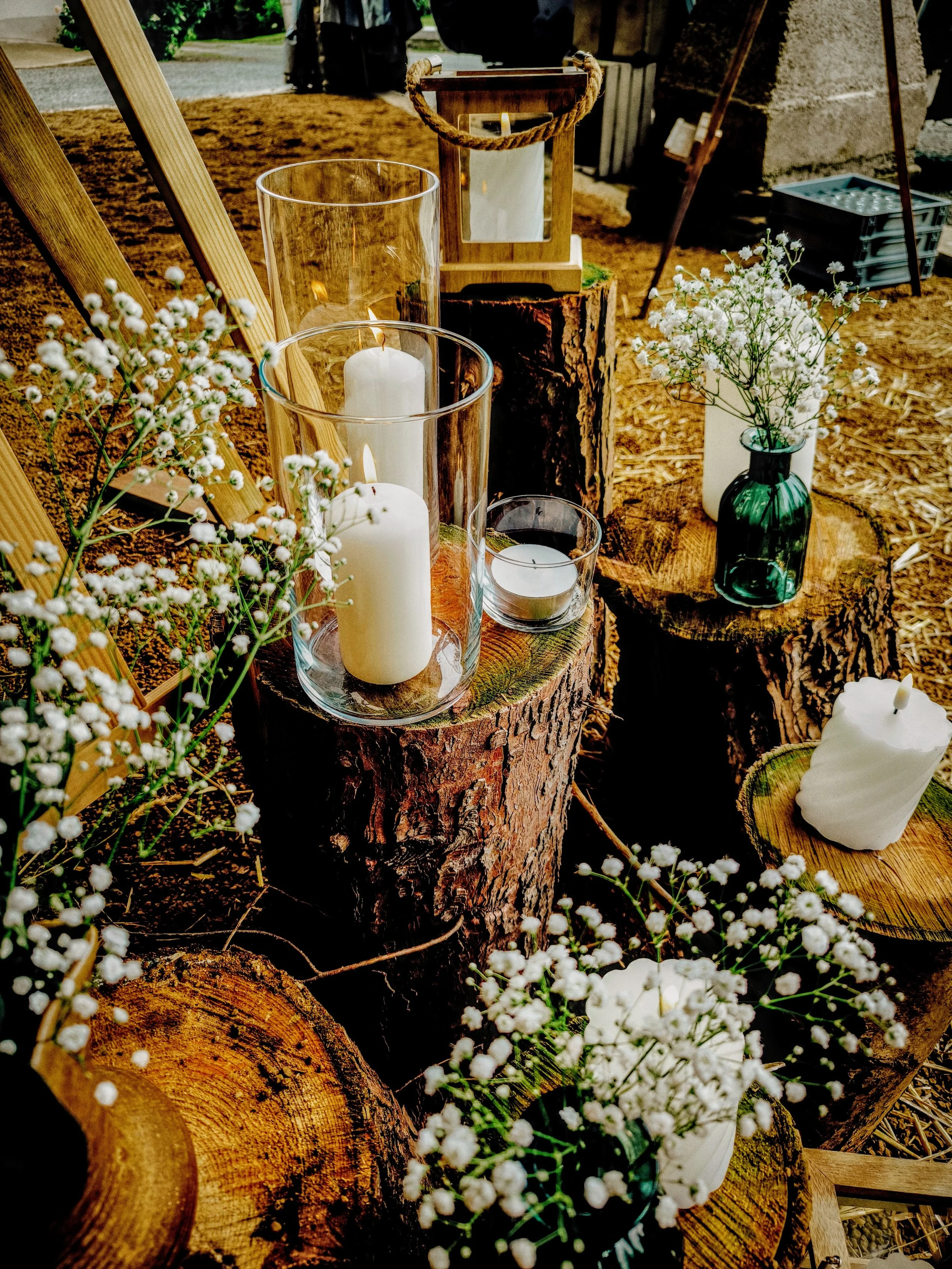 Décoration rustique avec bougies blanches dans des vases en verre, fleurs blanches dans des vases en verre vert, sur des rondins de bois naturels.