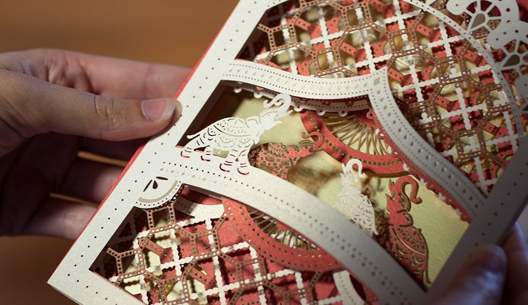 Close-up of a paper craft with intricate cutouts, including an elephant and decorative patterns, held by a person's hand.