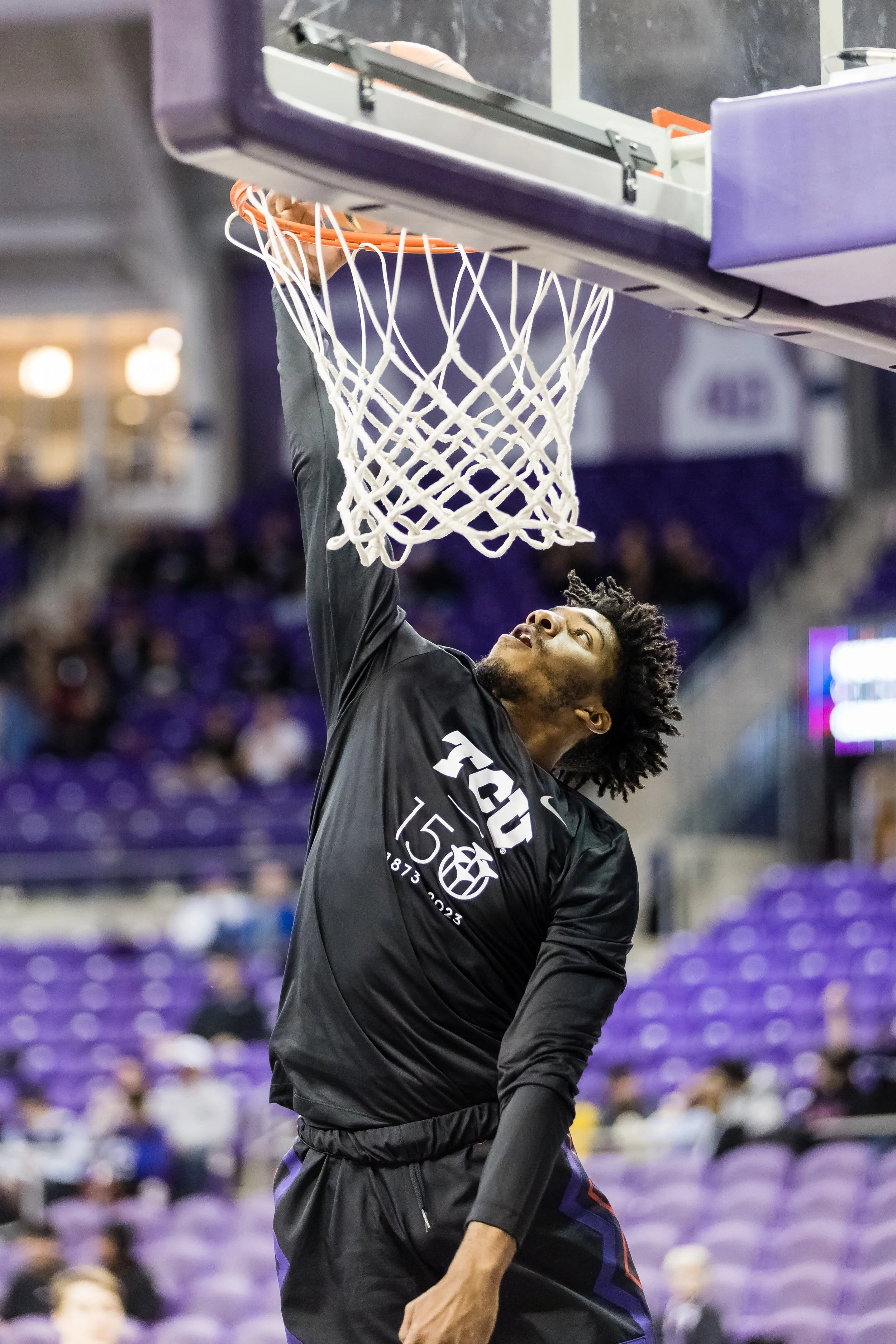A basketball player in black practice gear is dunking a basketball into the hoop during warm-up or practice.