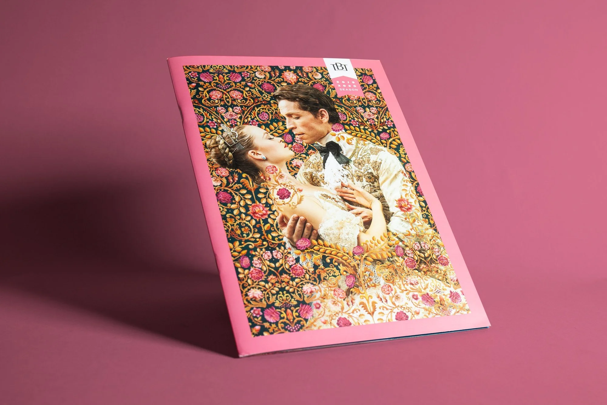 Magazine cover with a man and woman in vintage wedding attire, facing each other and touching, against a richly embroidered floral background.