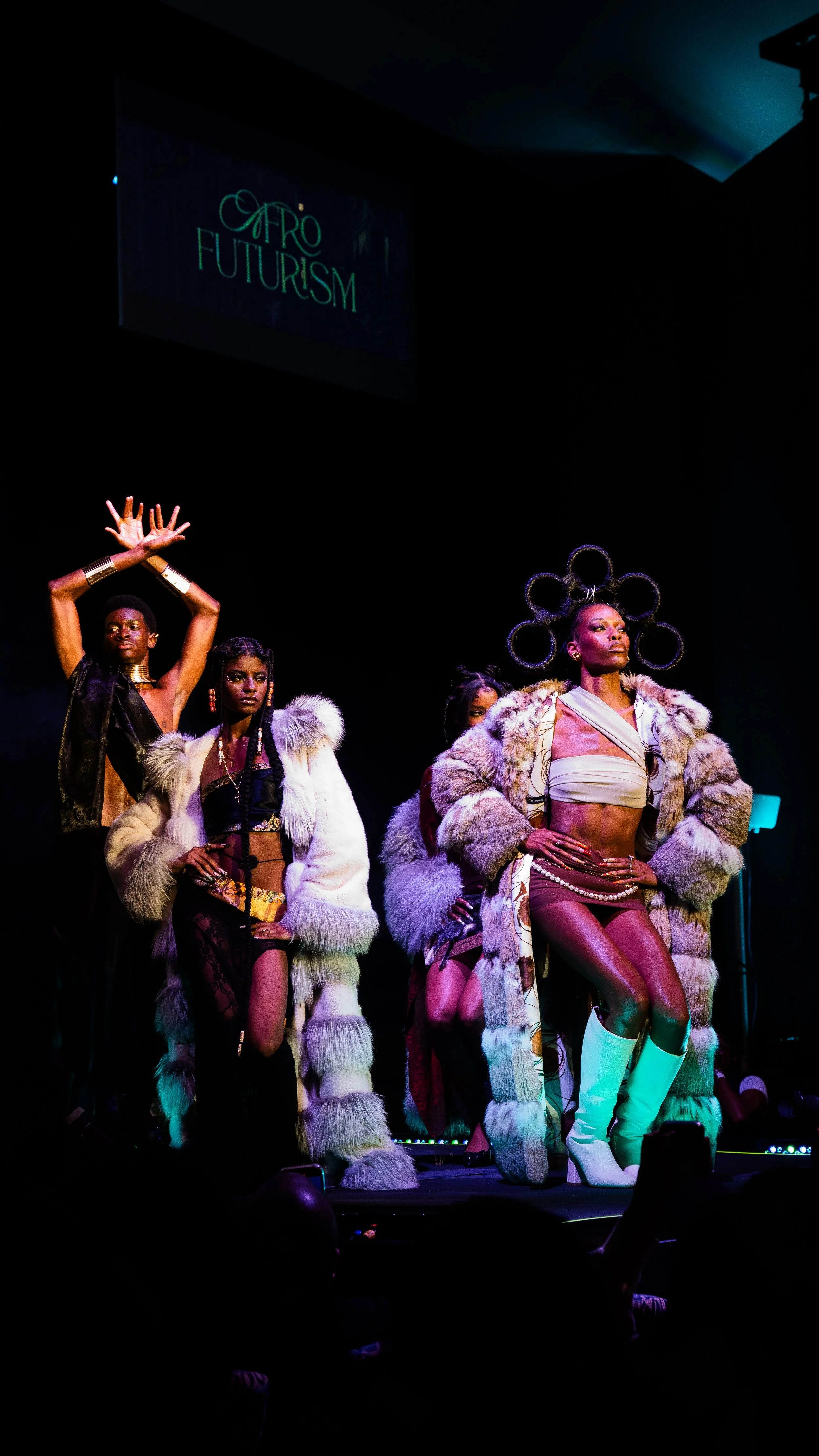 Fashion models on stage during a runway show titled Afro Futurism, wearing bold, futuristic outfits and accessories inspired by African culture and sci-fi themes.
