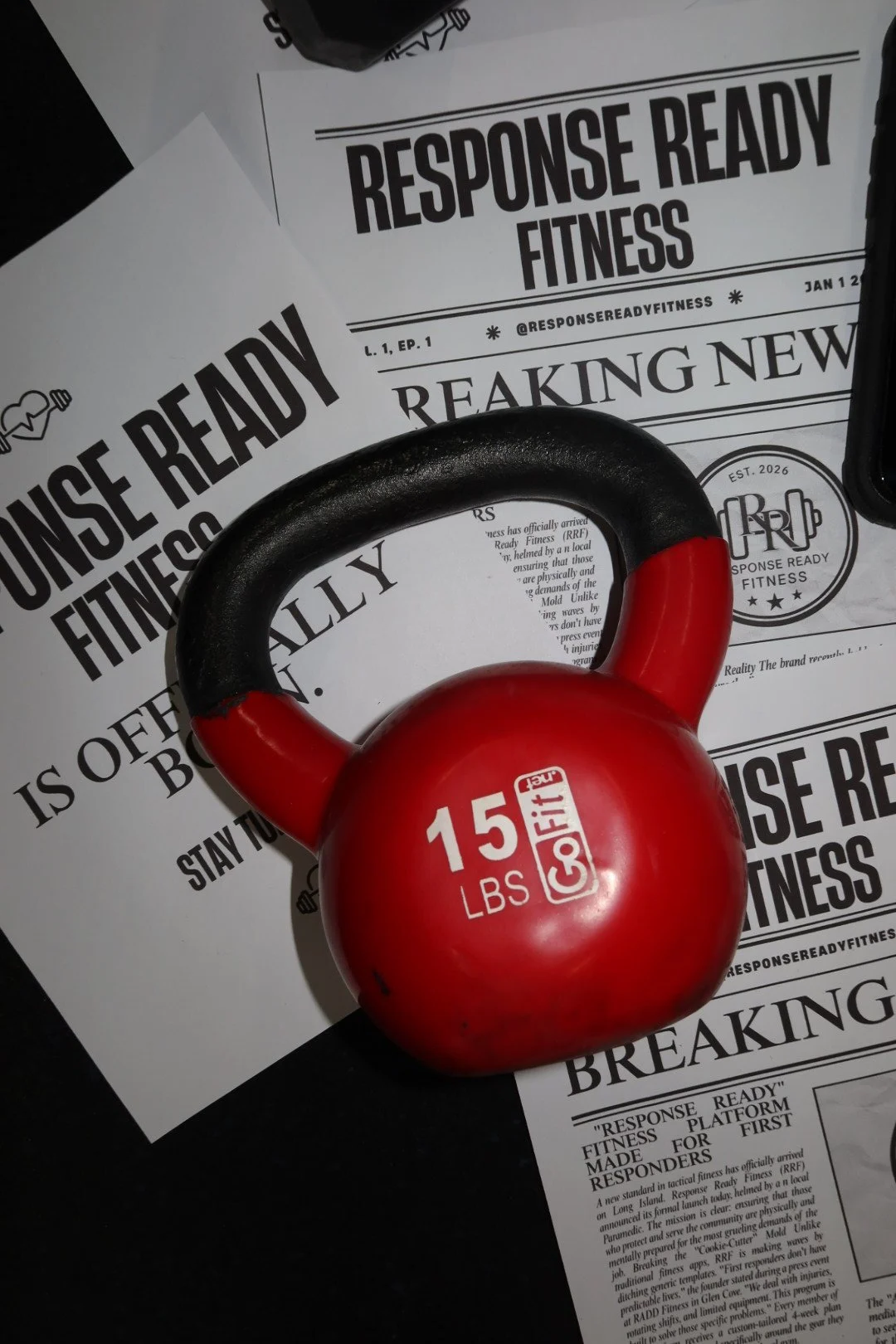 A red 15-pound kettlebell placed on top of fitness newspapers with bold headlines about Response Ready Fitness.