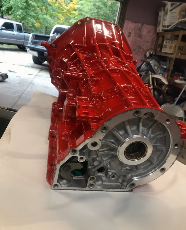 Red painted automotive transmission case on work surface in a garage or workshop.