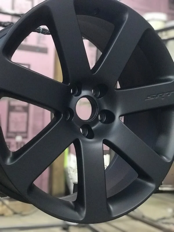 A black car wheel rim with five spokes, displayed vertically in a store or workshop.