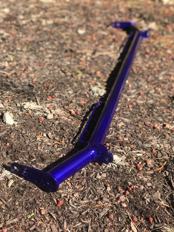 A blue bicycle kickstand lying on a dirt ground with small rocks and dried leaves.