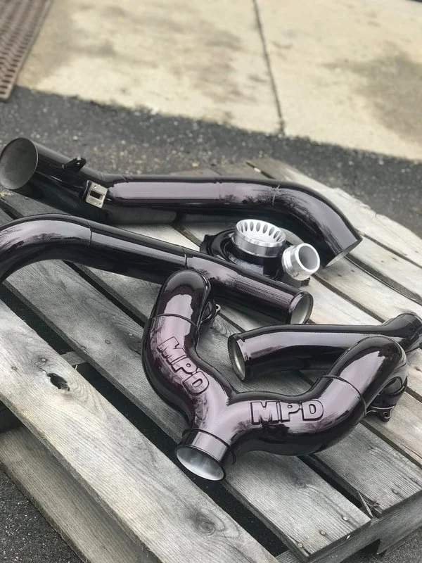 Set of black turbo pipes with silver fittings on a wooden pallet outdoors.