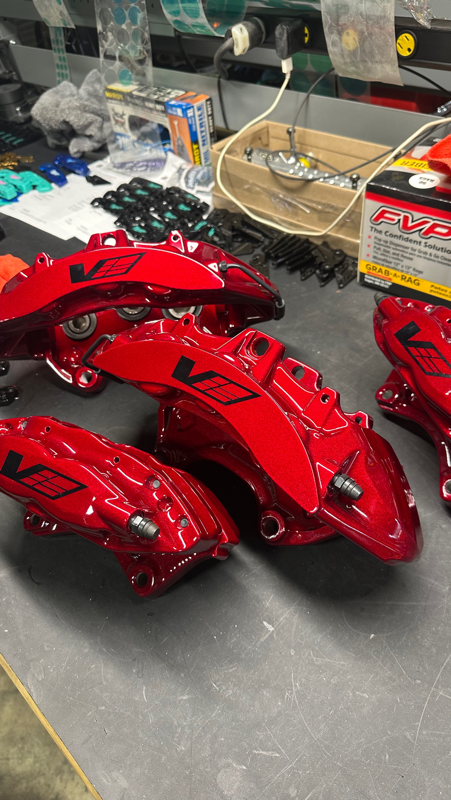 Four red and black brake calipers with the VBC logo on a workbench in a workshop.