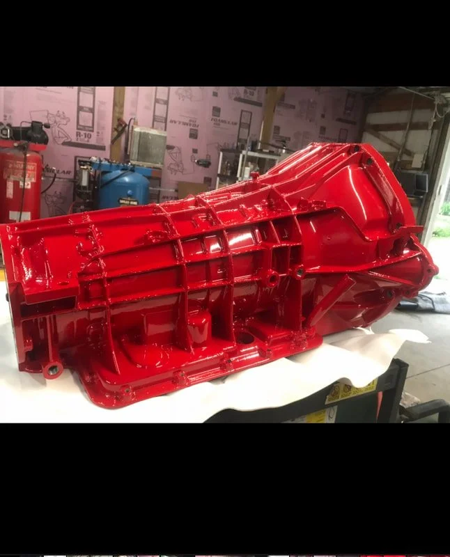Red painted engine component in a garage or workshop with tools and equipment in the background.